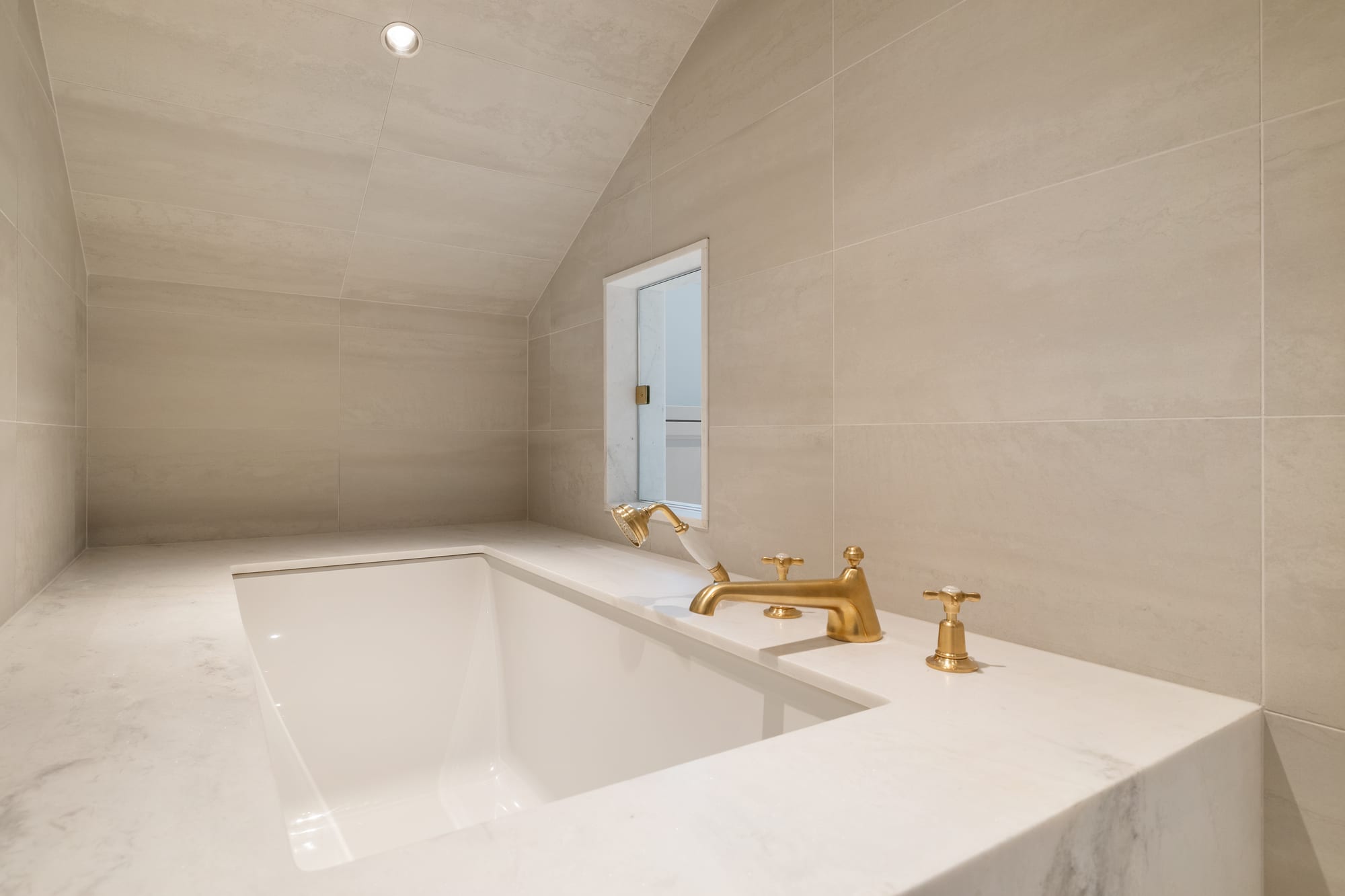 Bath with undermount tub, marble deck and full-height stone tile walls.