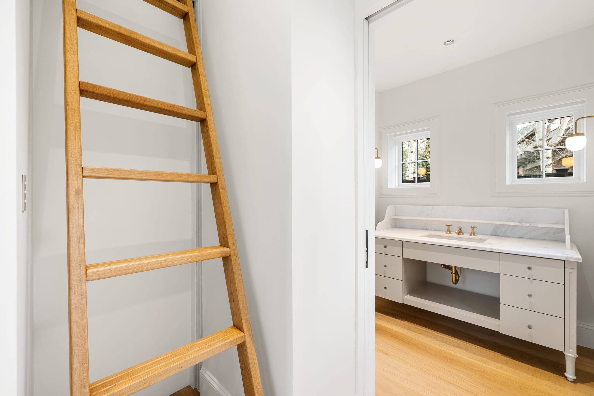 White oak library ladder beside the powder vanity in painted cabinetry.