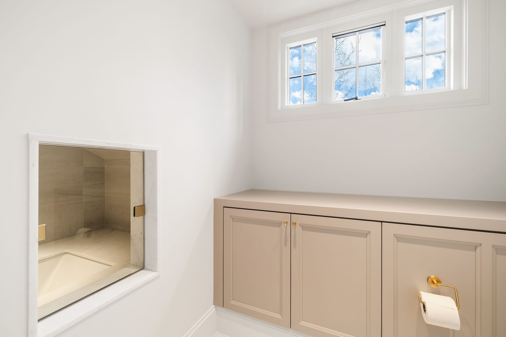 Painted bath cabinetry with brass hardware and an interior window to the shower.