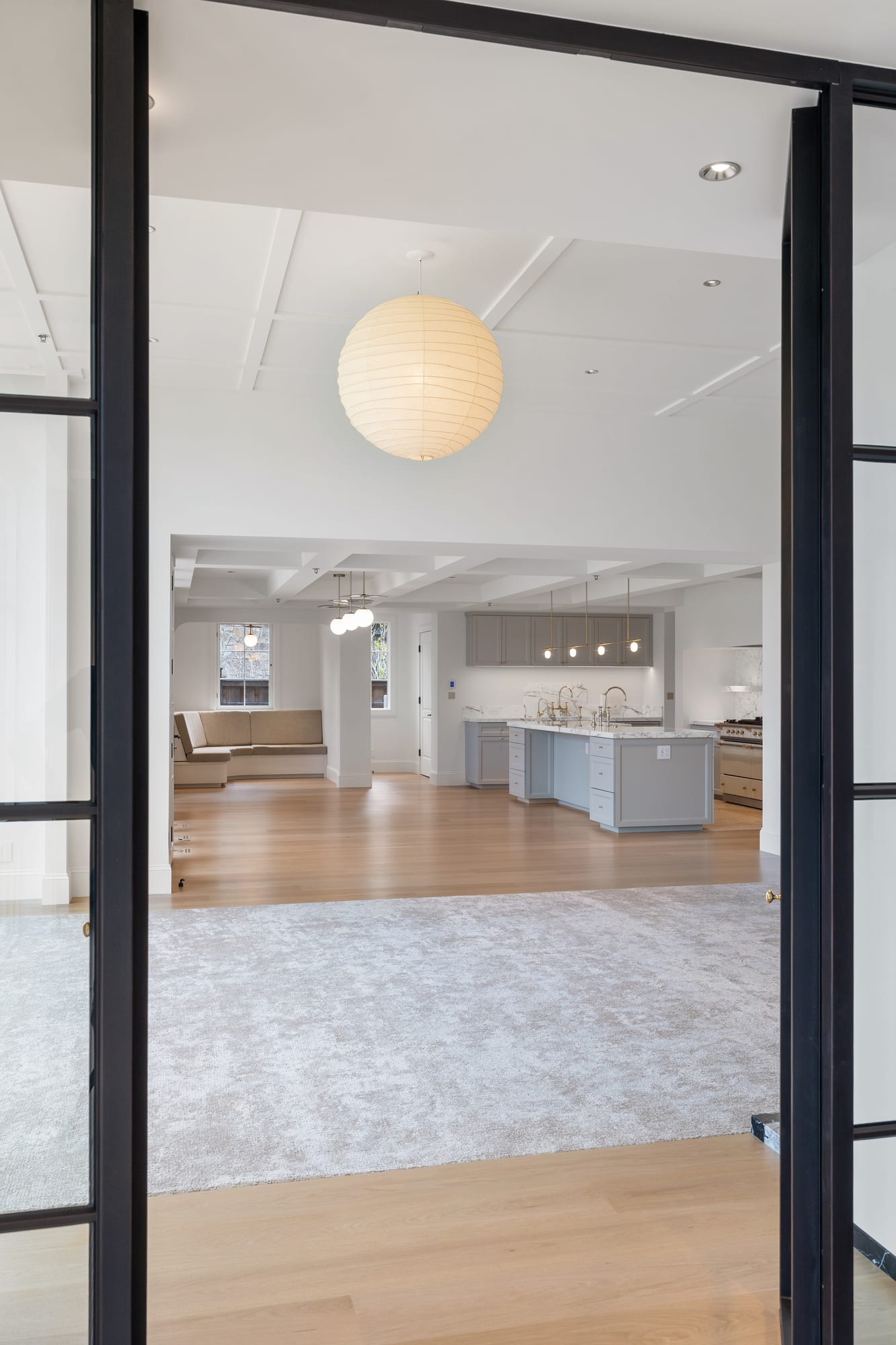 View from the great room through black steel doors into the painted kitchen.