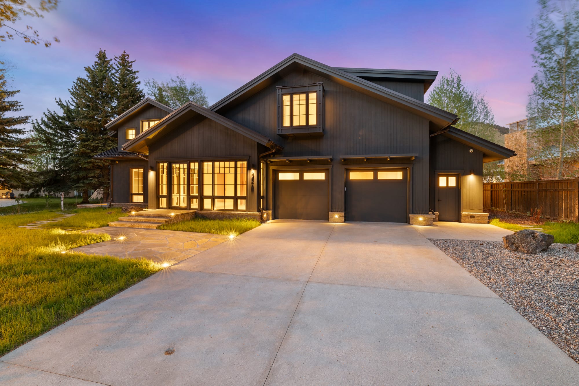 Dusk driveway approach with the garage wing and lit entry.