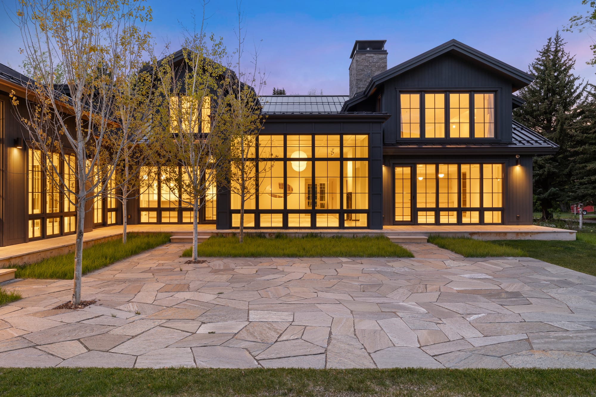 Dusk patio with chimney and lit window walls across the flagstone.