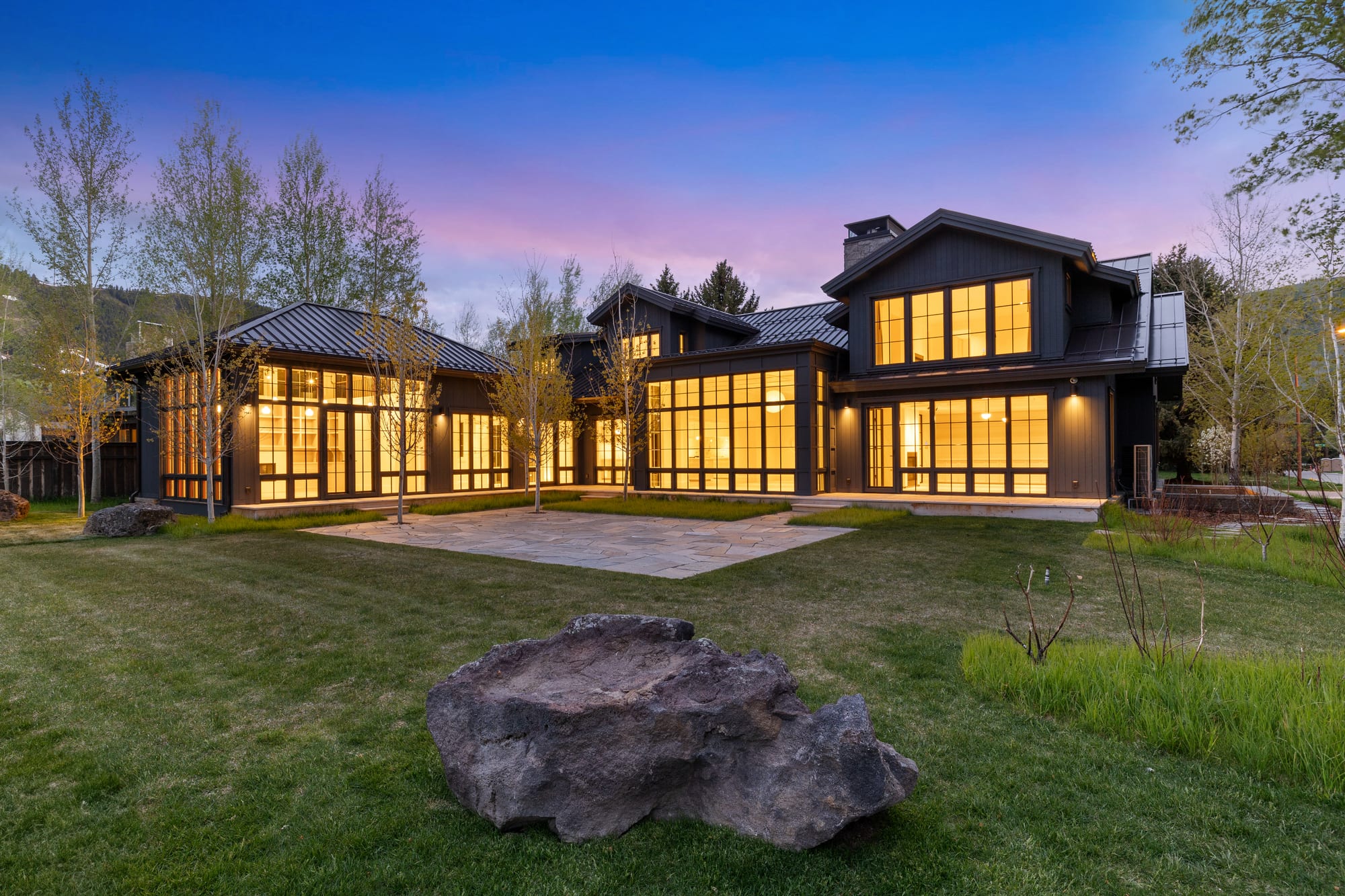 Dusk rear elevation with boulder landscape and lit windows.