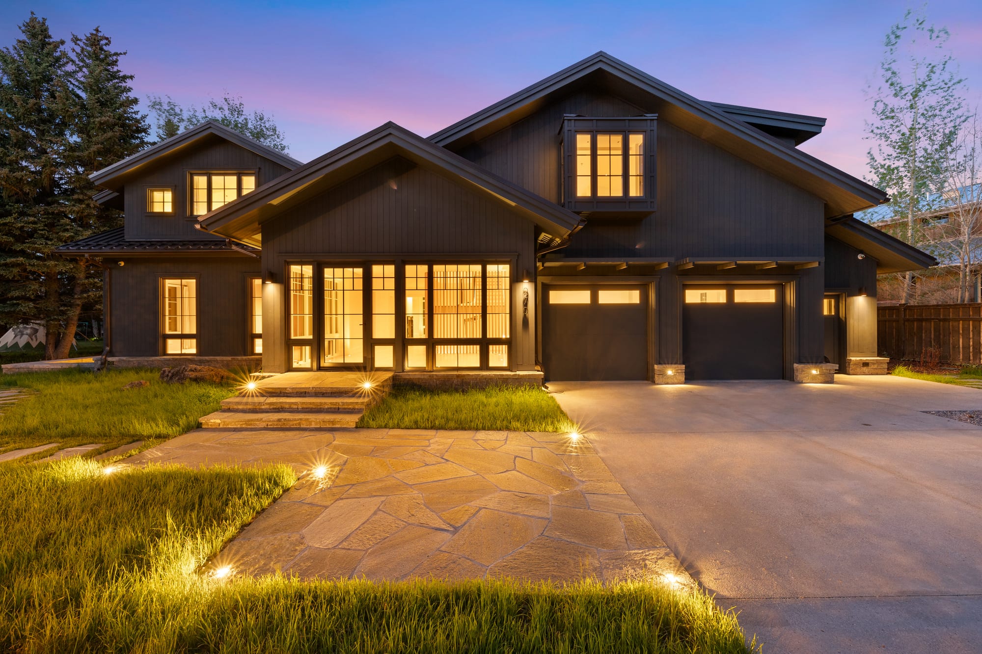 Dusk front elevation with garage doors and stone drive court.