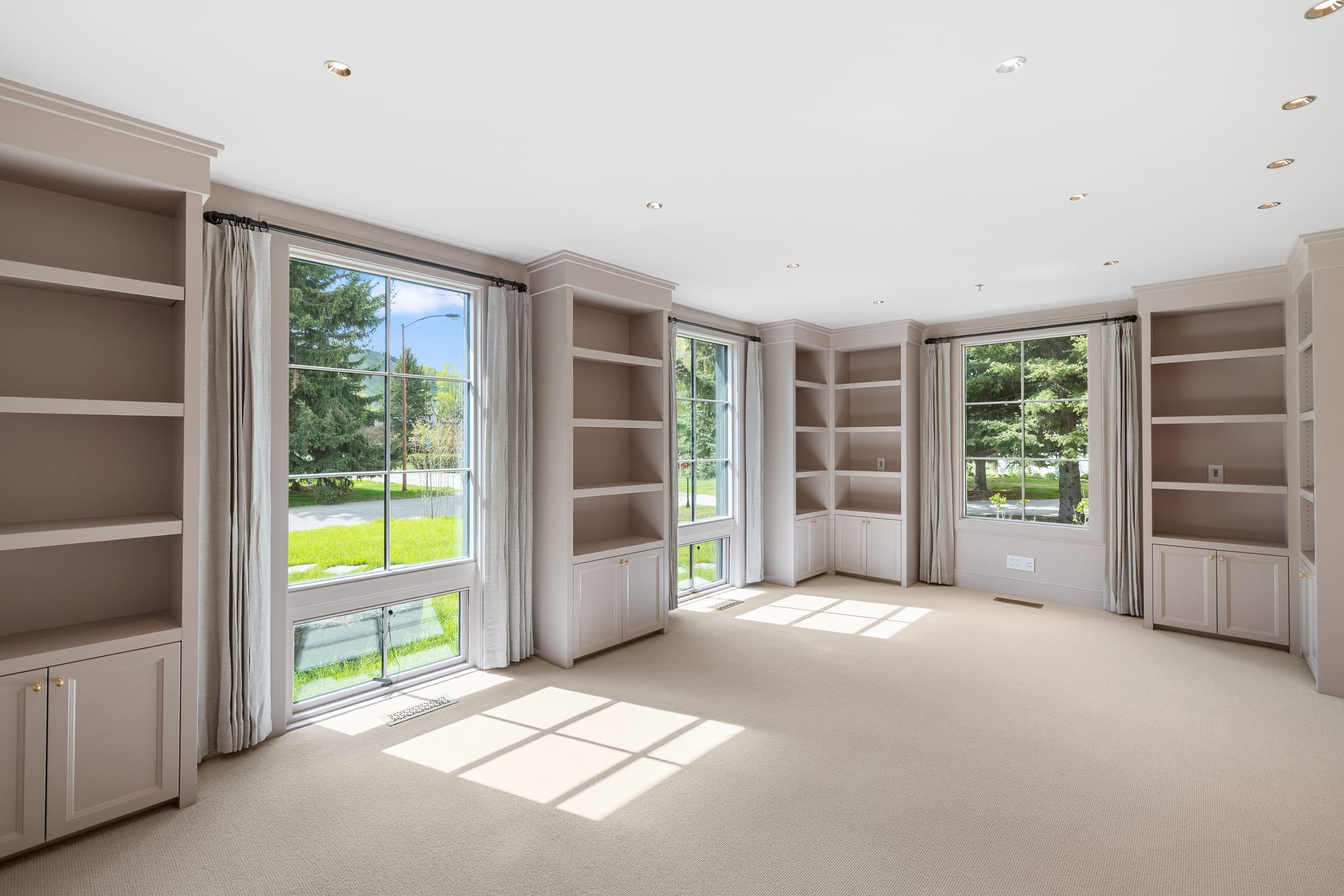 Study lined with painted built-in bookcases running between three window bays.