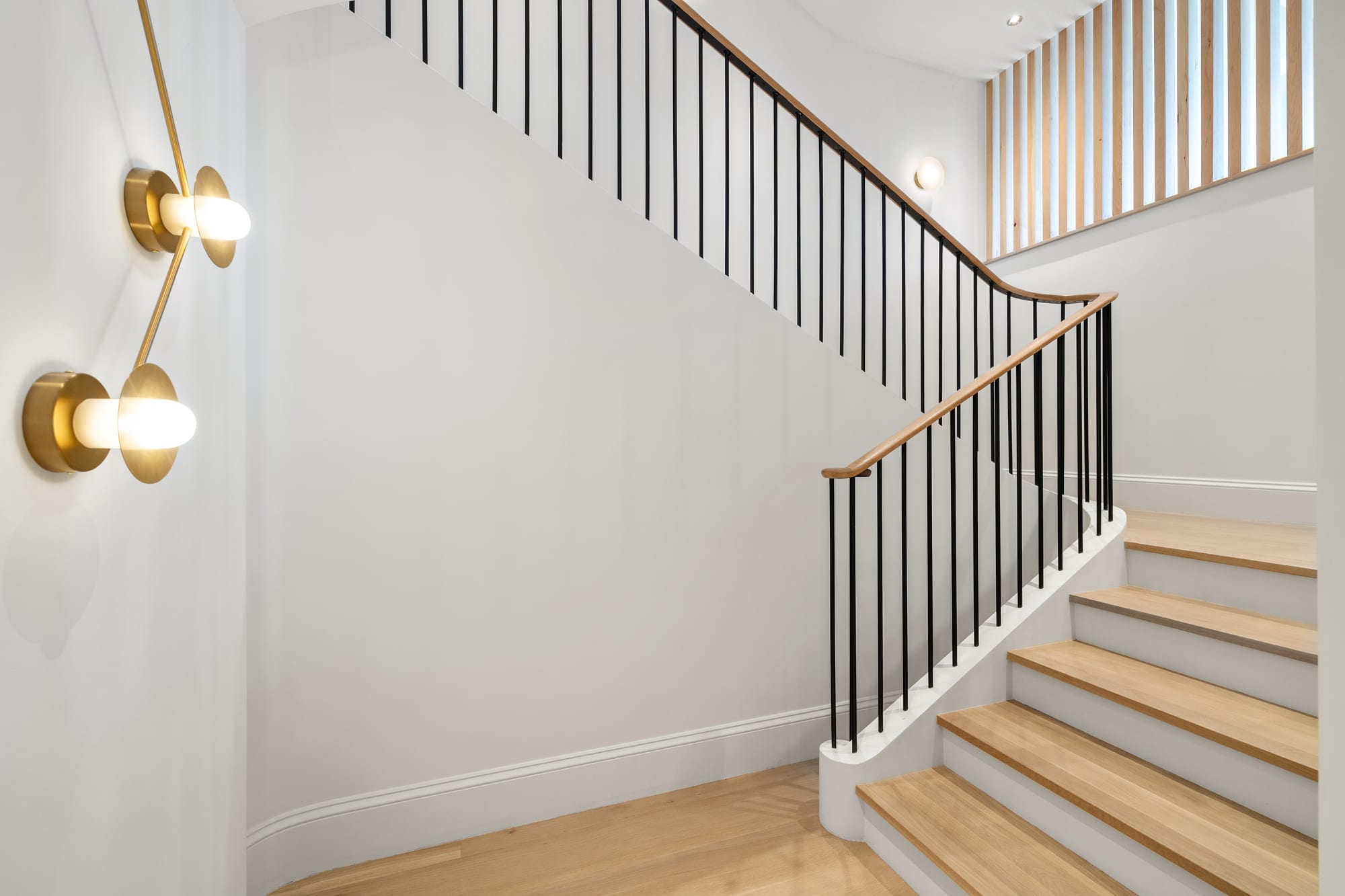 The angled stair — oak treads, black metal balusters, slat wall above.