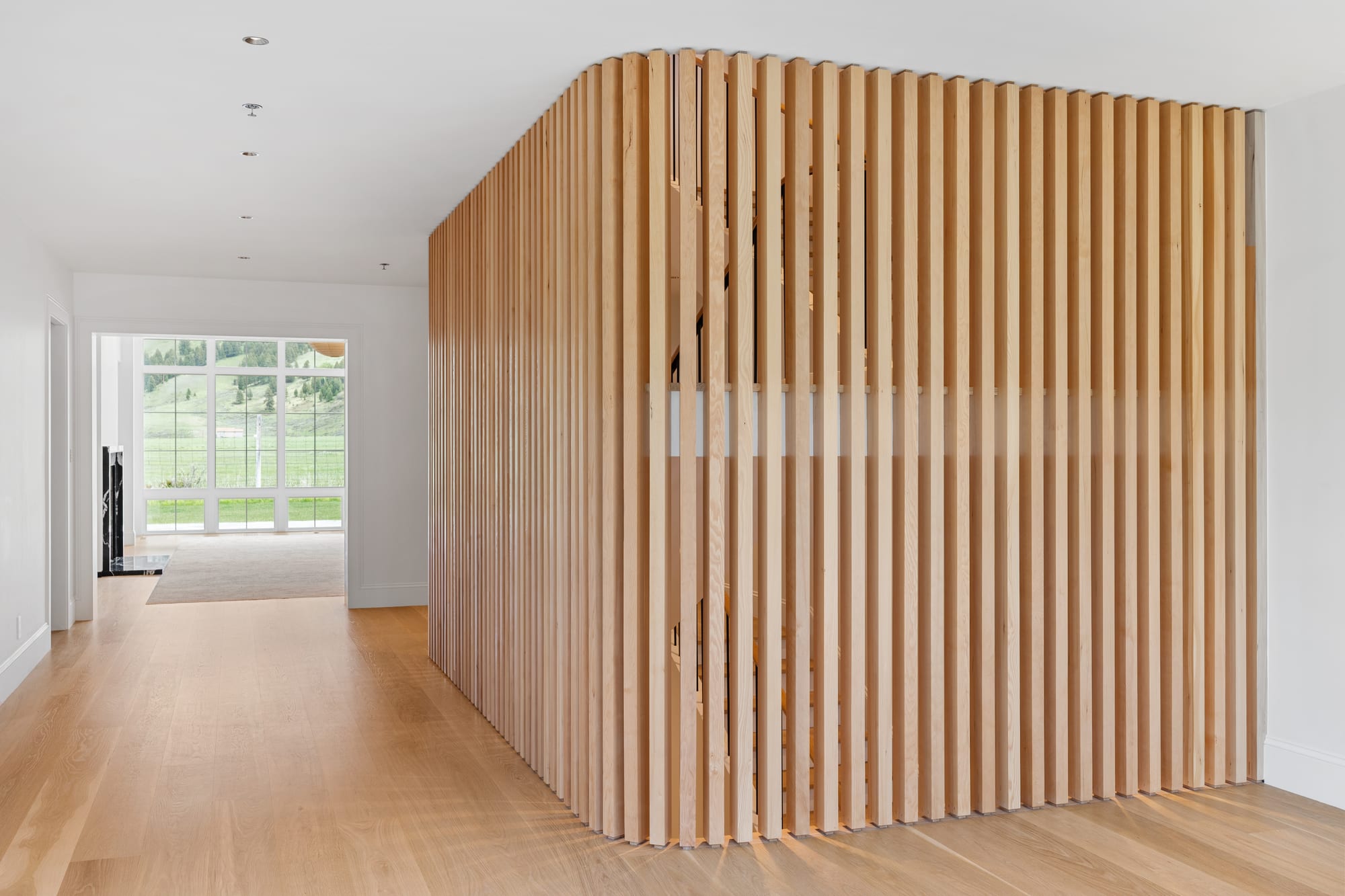 White oak slat screen dividing the entry from the great room, over wide-plank oak floors.