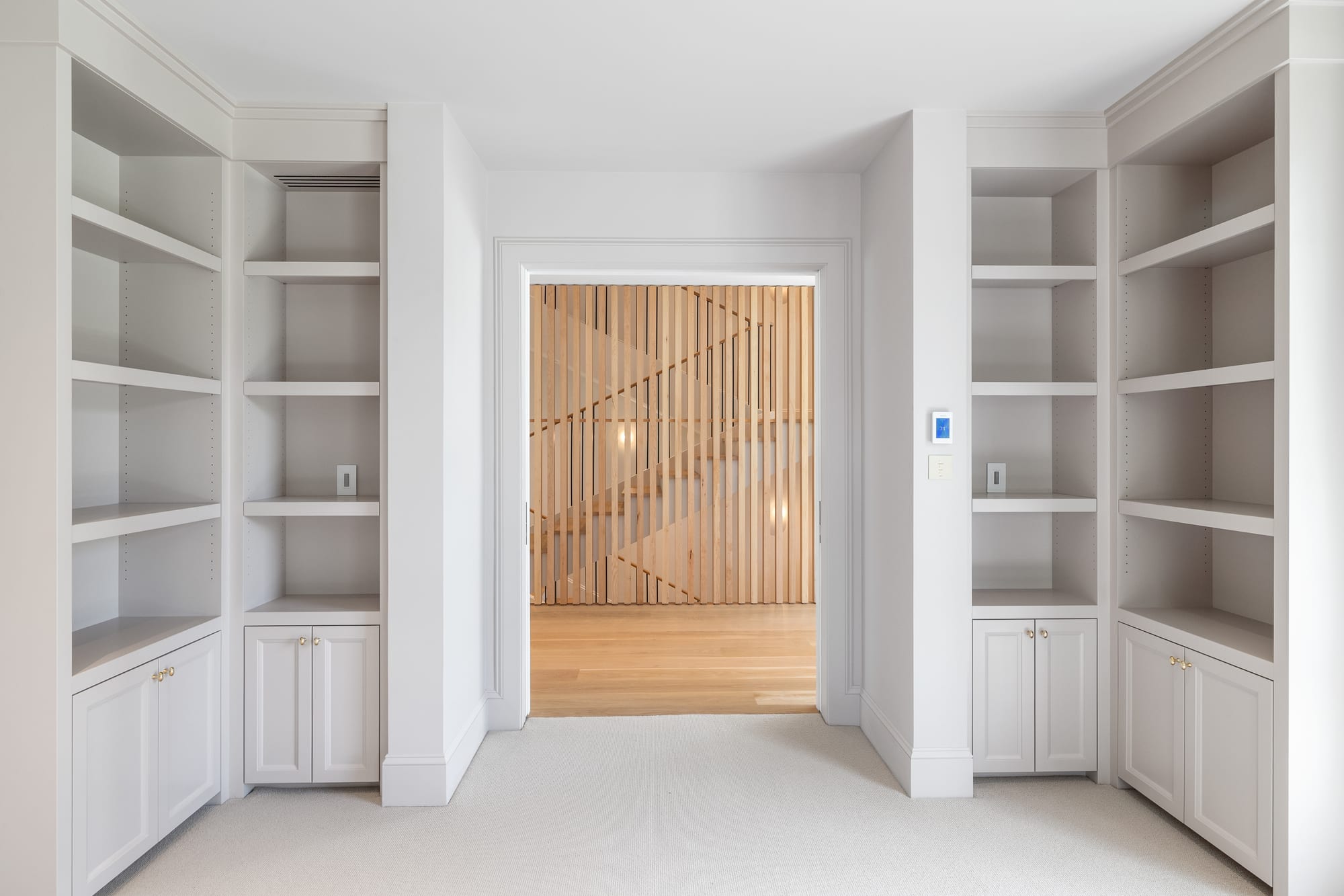Symmetrical painted bookcases flanking the doorway to the oak slat stair hall.