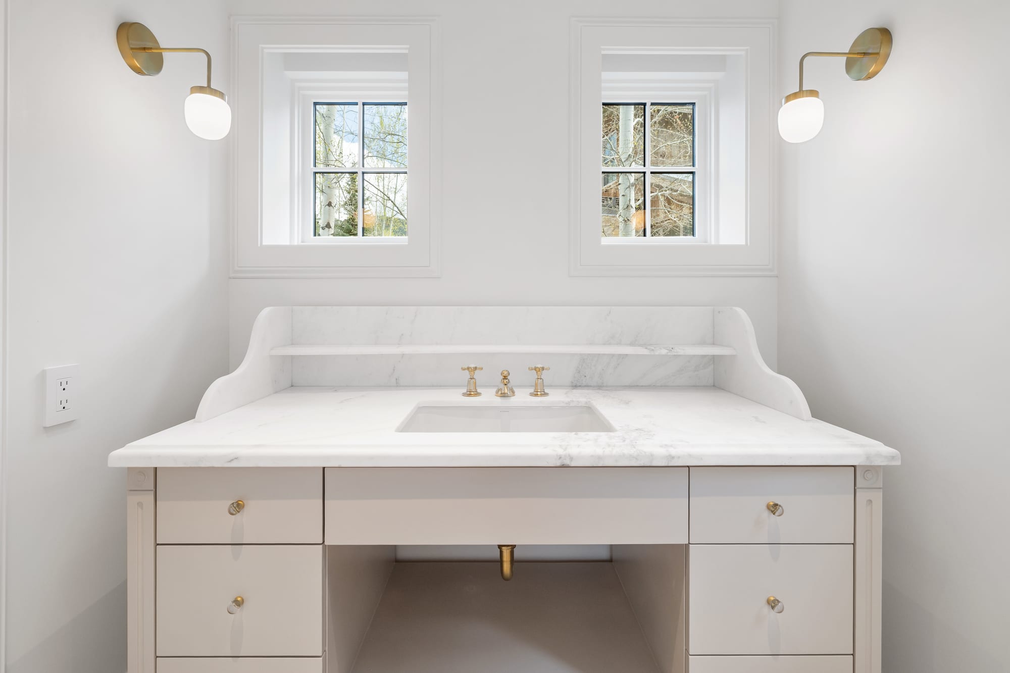 Powder vanity in painted cabinetry with shaped marble backsplash and brass fittings.