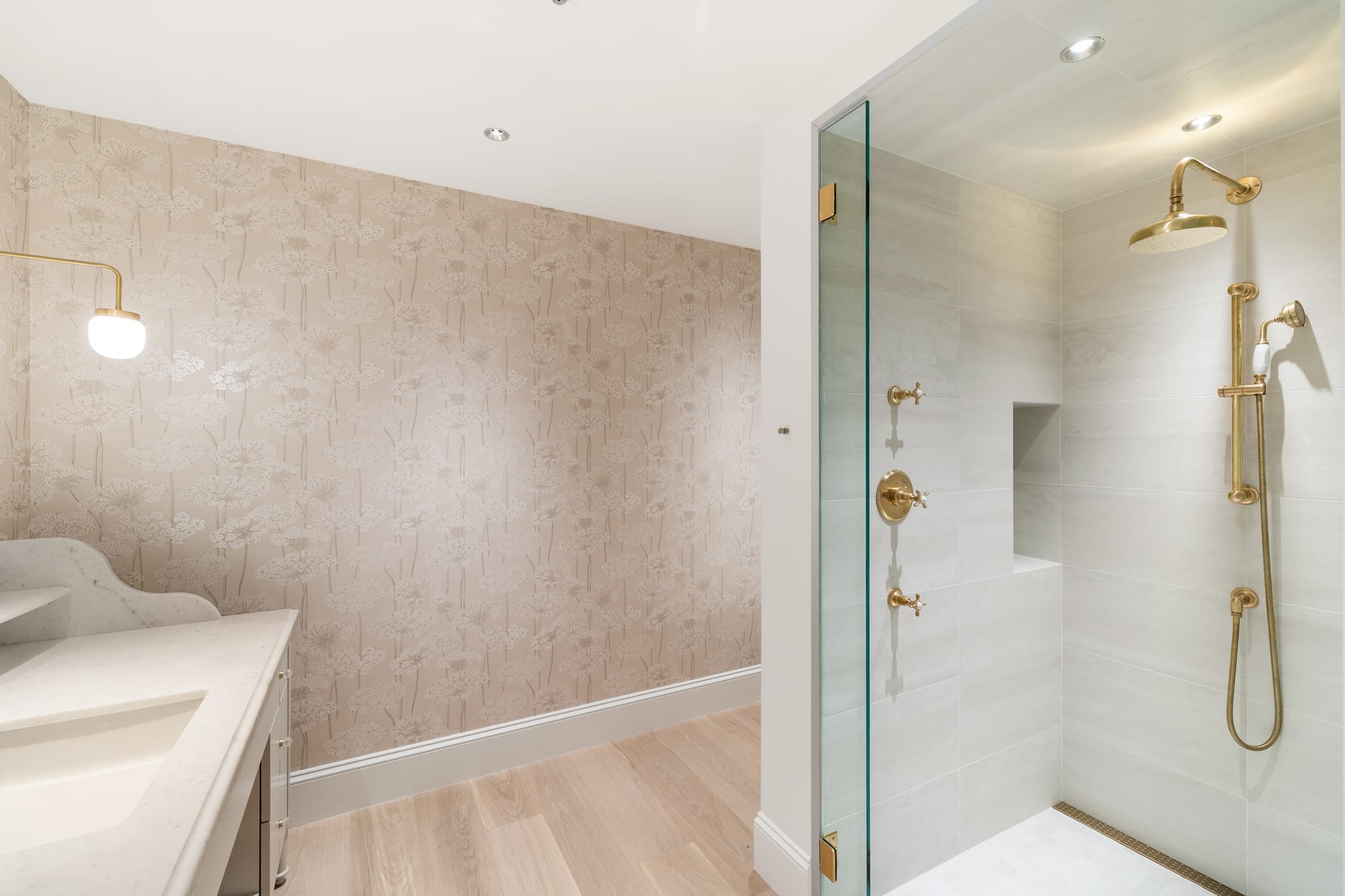 Guest bath with shaped marble backsplash, wallpaper and brass-trimmed glass shower.