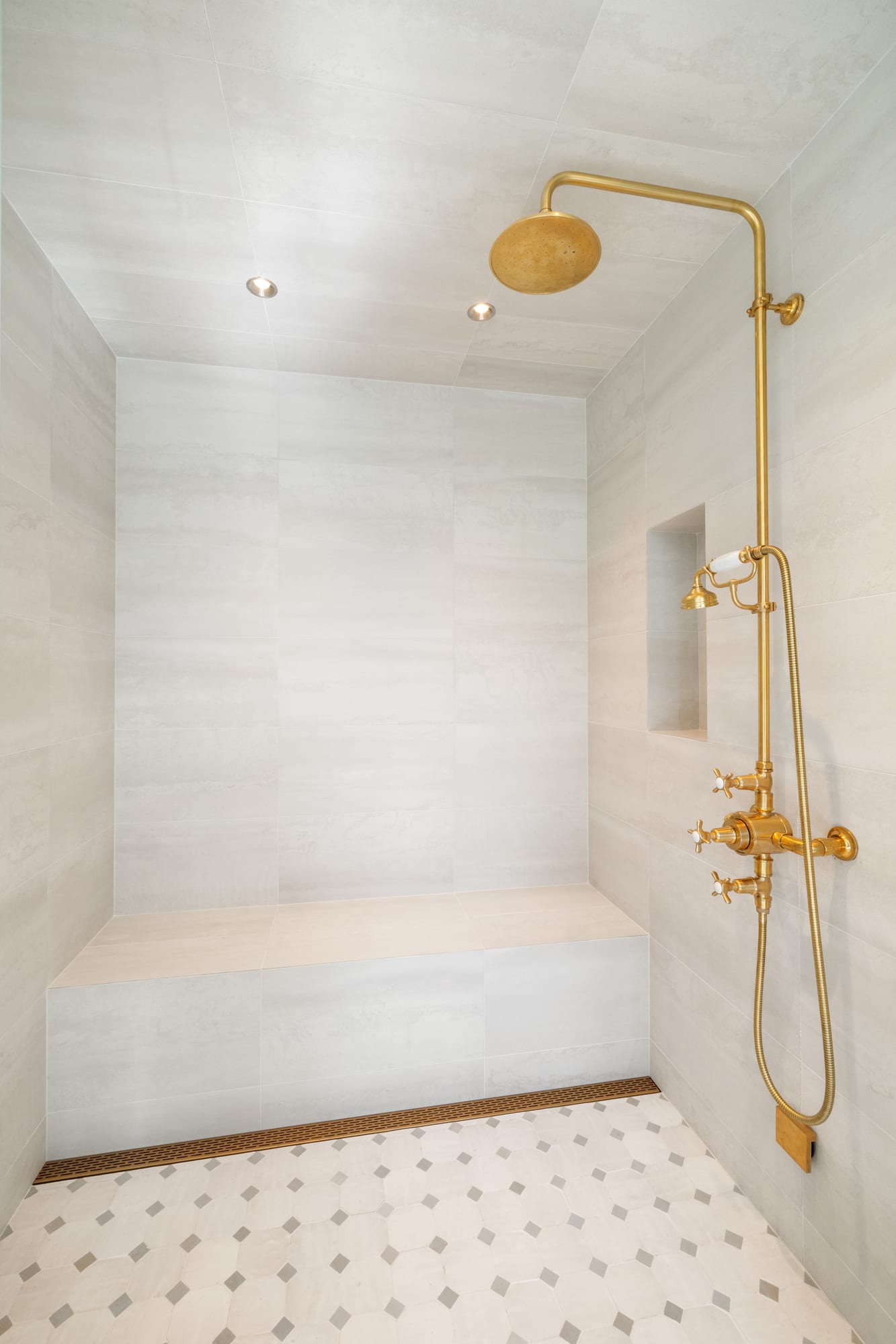 Walk-in shower in large-format stone with a bench and unlacquered brass fittings.