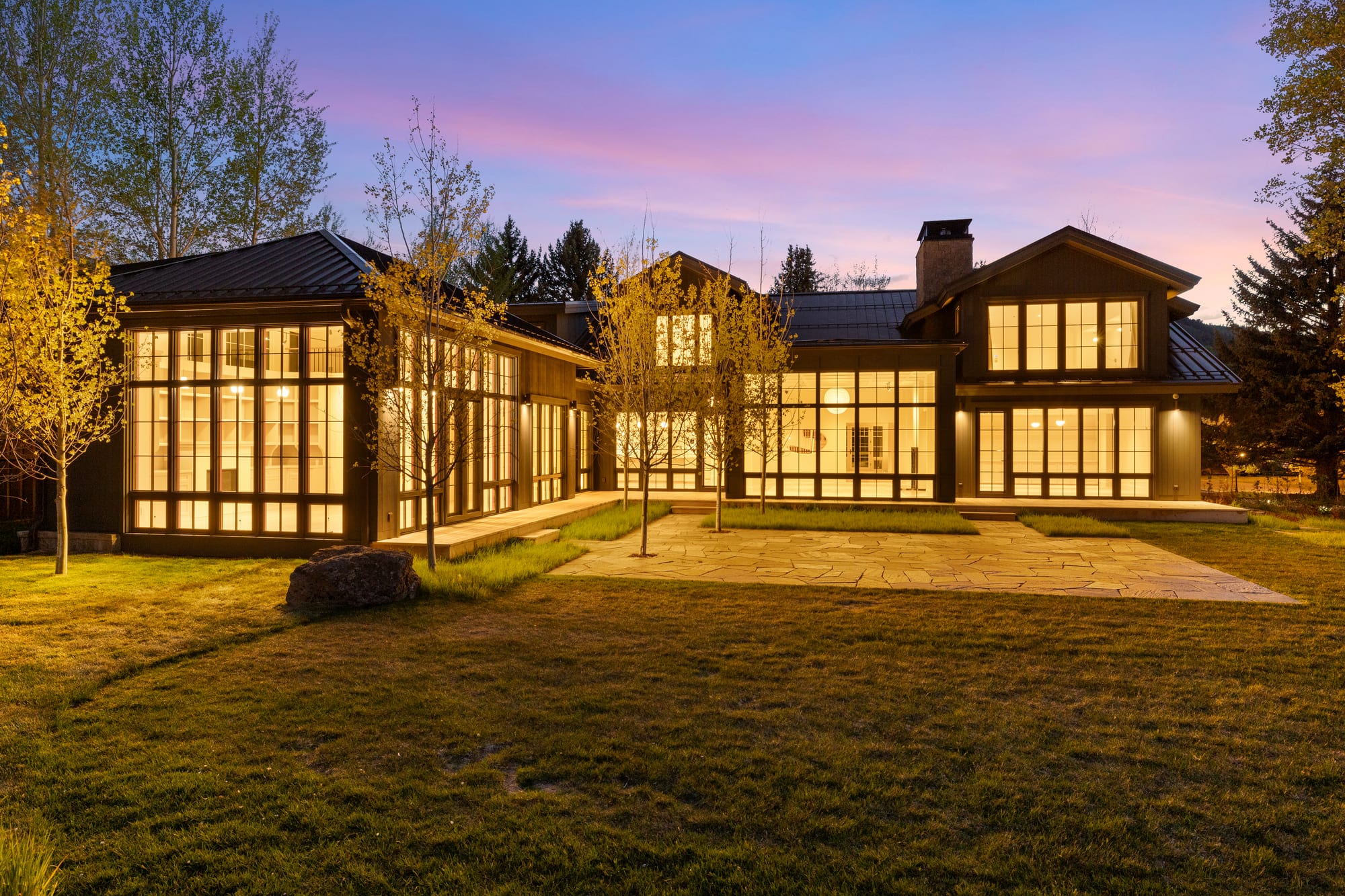 Rear elevation at dusk, window walls lit across the flagstone patio.
