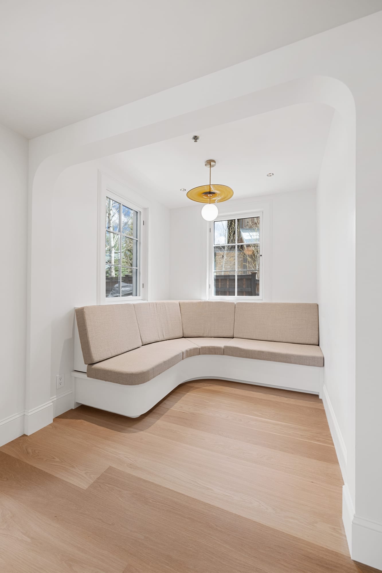 Curved upholstered banquette built into a plaster dining nook under a brass pendant.