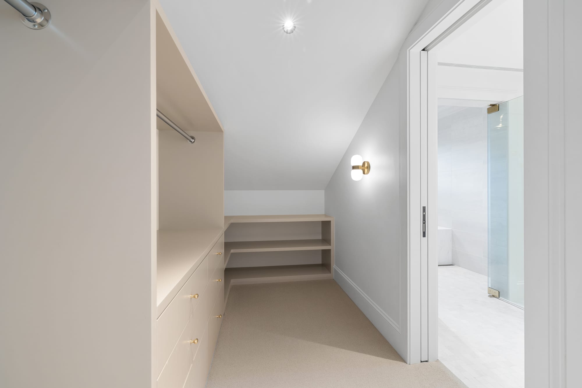 Closet under a sloped ceiling with painted drawer bank and open shelving.