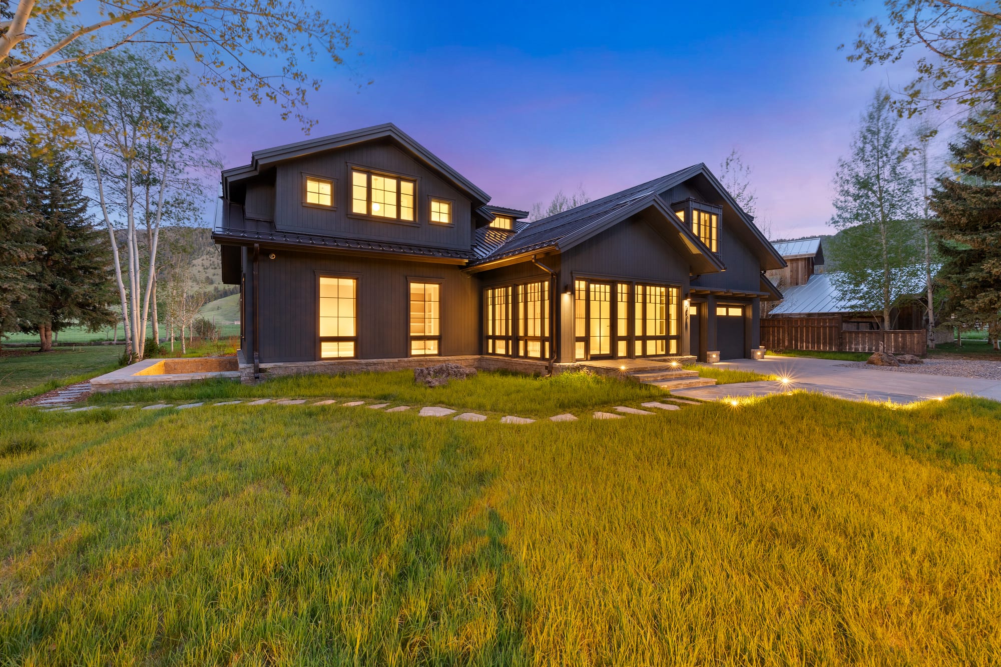 Dusk side elevation across the lawn with lit window walls.