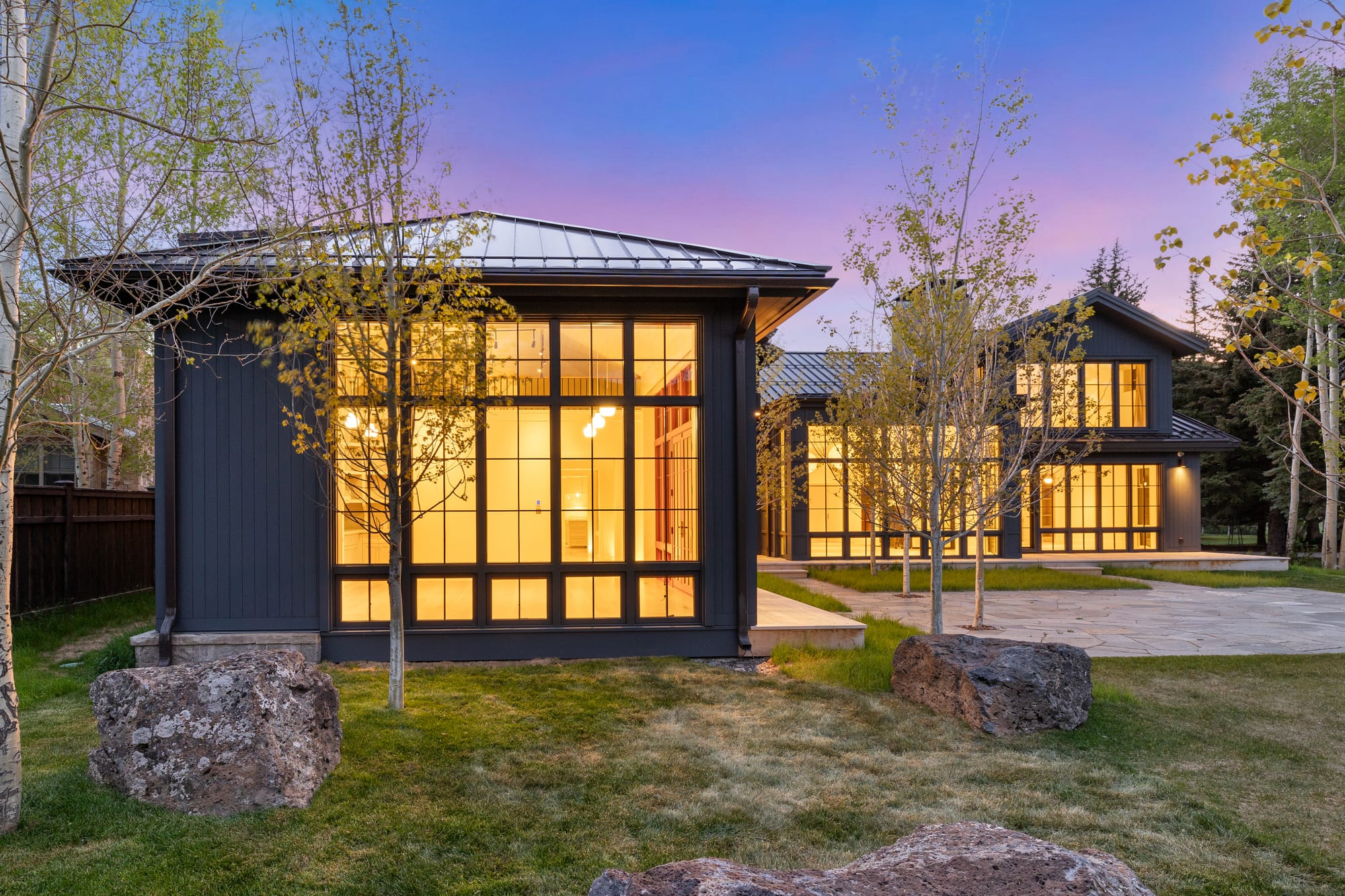 The studio pavilion glowing at dusk beside the courtyard lawn.