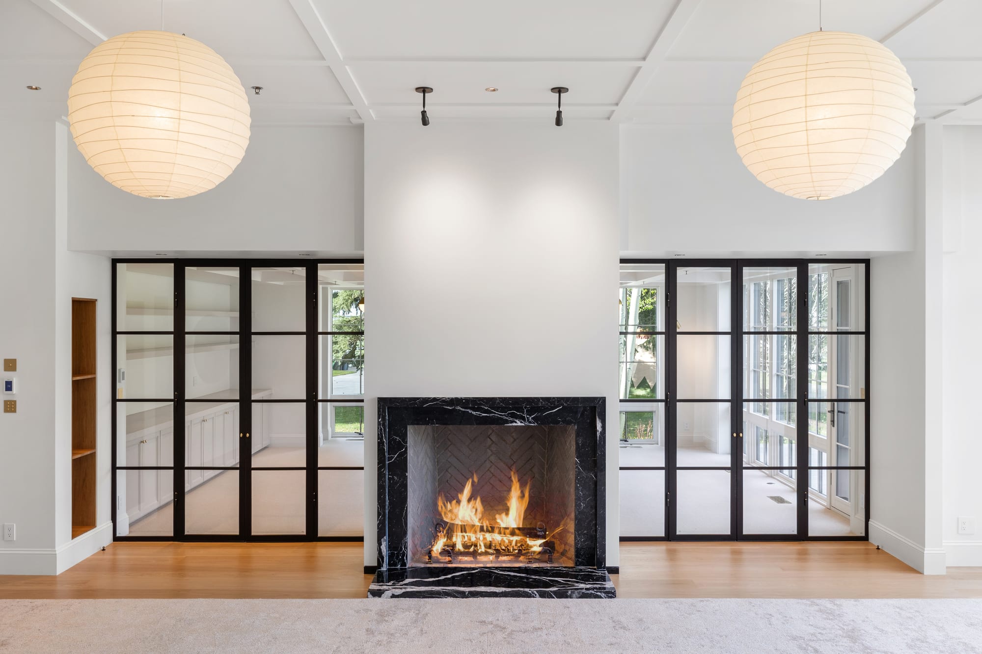 Great room hearth in black marble between paired steel doors and globe pendants.