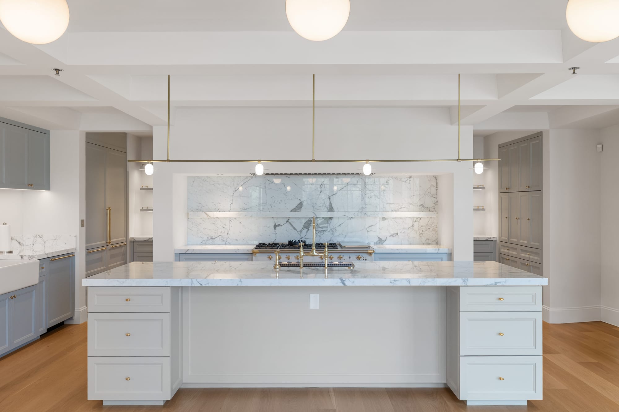 Painted kitchen with full-height marble slab backsplash, brass fittings and a marble island.