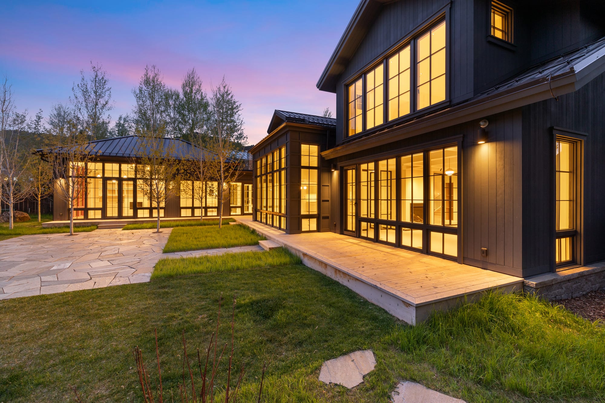 Dusk courtyard with cedar deck running the length of the lit window wall.