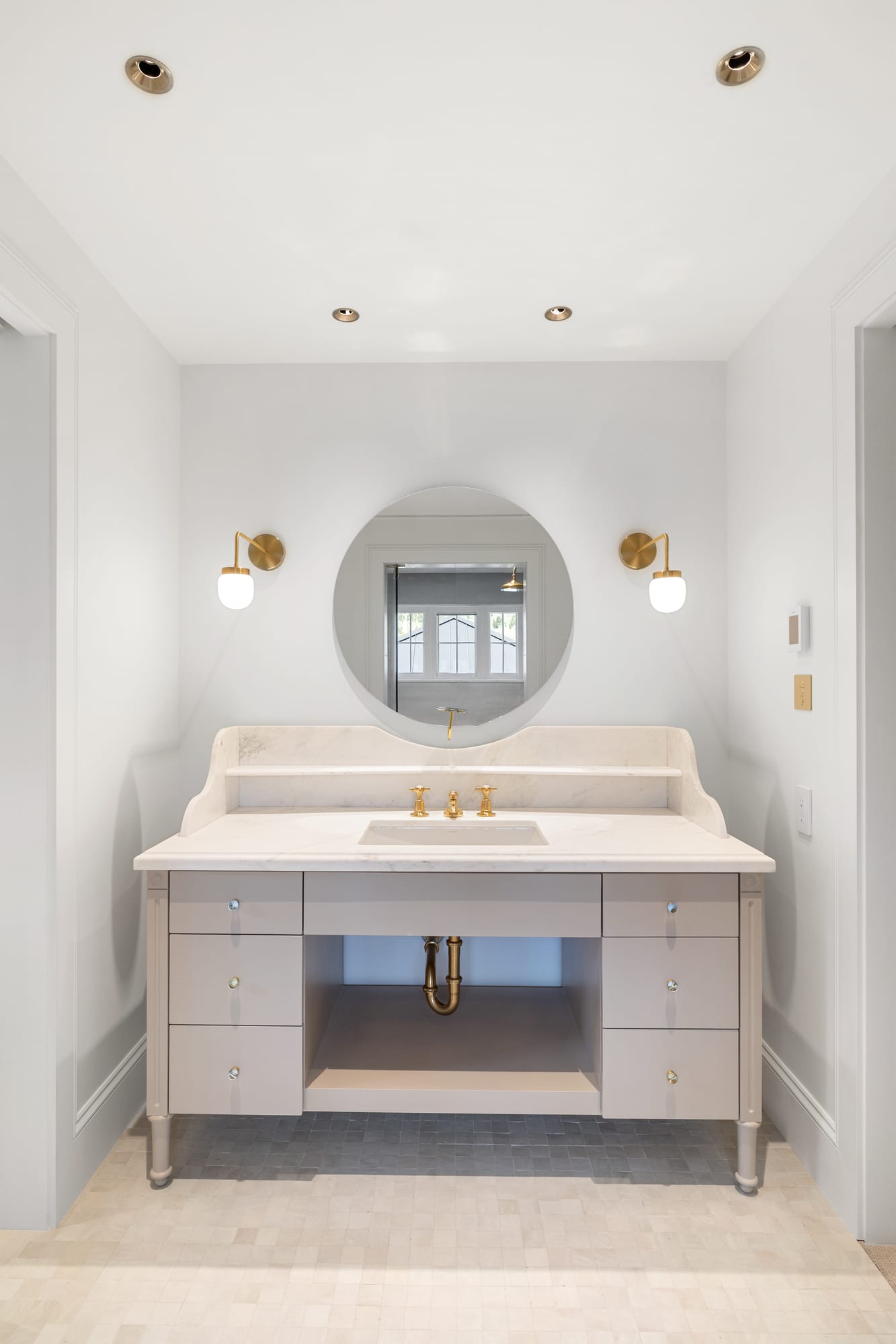 Powder room with marble vanity, oval mirror and unlacquered brass sconces.