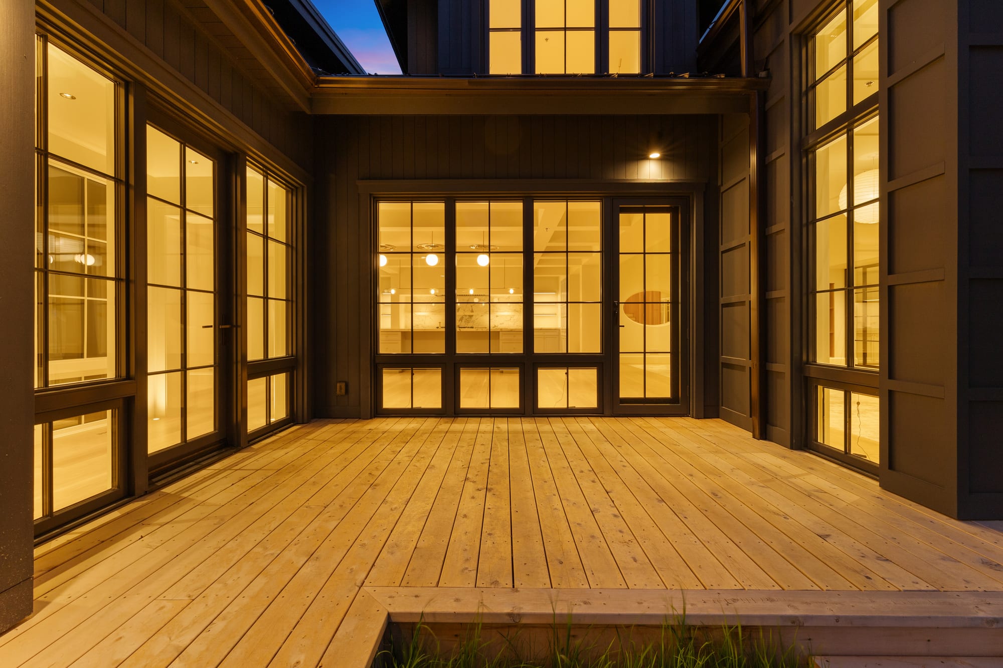 Cedar deck at dusk enclosed by steel window walls on three sides.