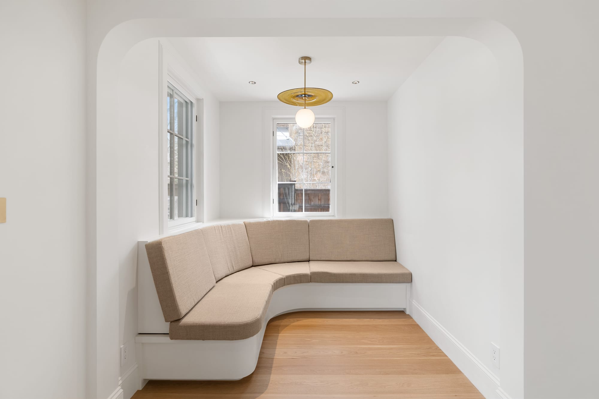 Curved upholstered banquette in a plaster nook under a brass and glass pendant.