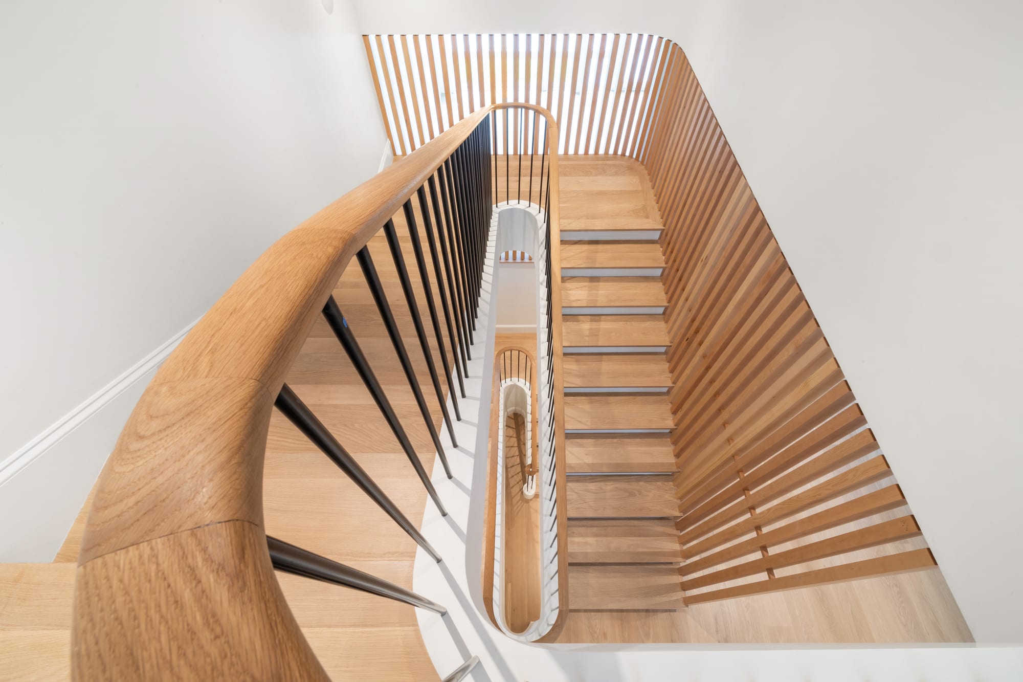 The angled stair from above — curved handrail, black balusters, white oak slat wall.