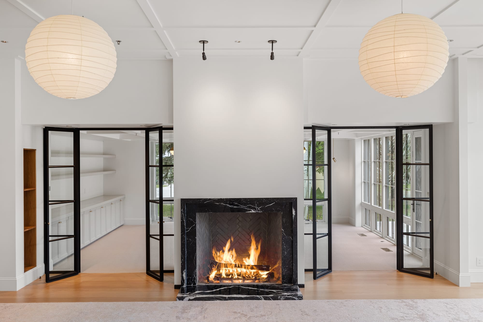 Great room hearth in black marble, flanked by steel doors and painted built-ins.