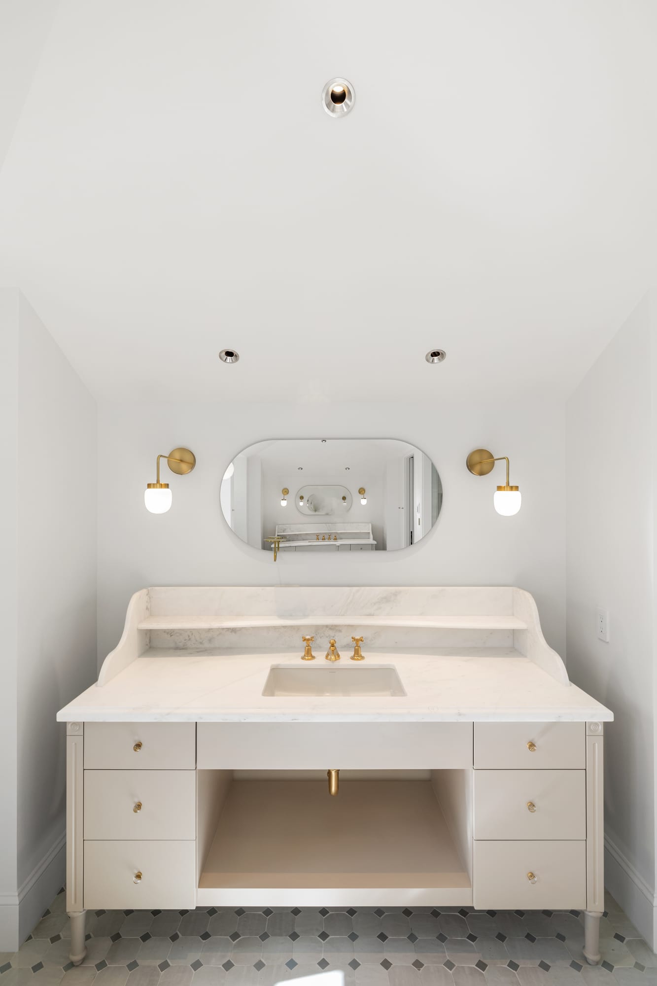 Powder room vanity in painted cabinetry with marble top and brass sconces.