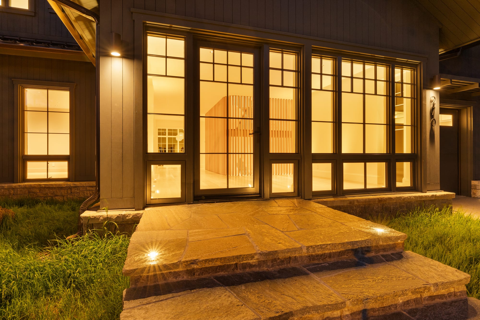 Entry at dusk — flagstone steps, steel doors, the lit slat wall inside.
