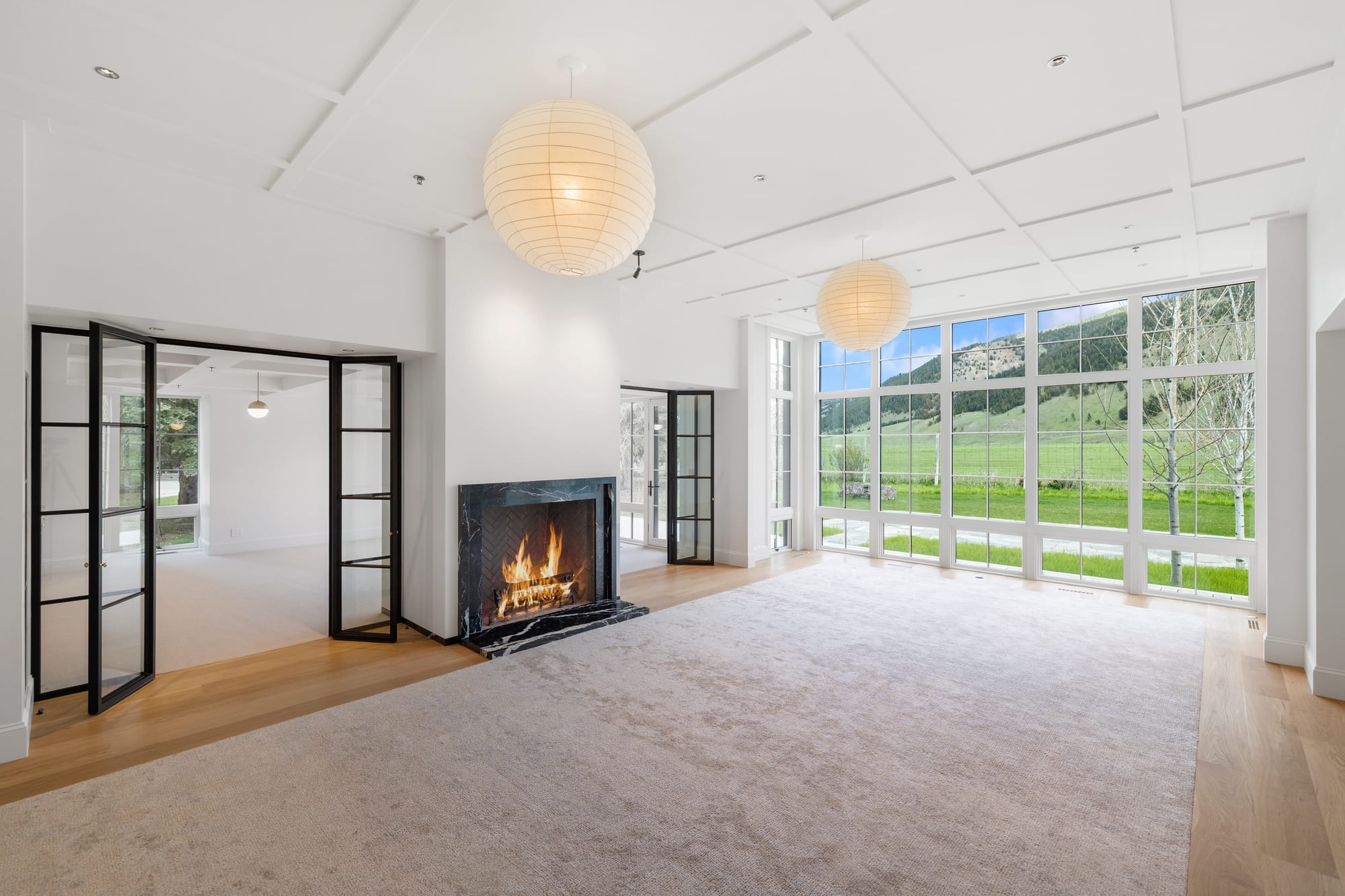 Great room with coffered ceiling, black marble fireplace and steel-framed french doors.
