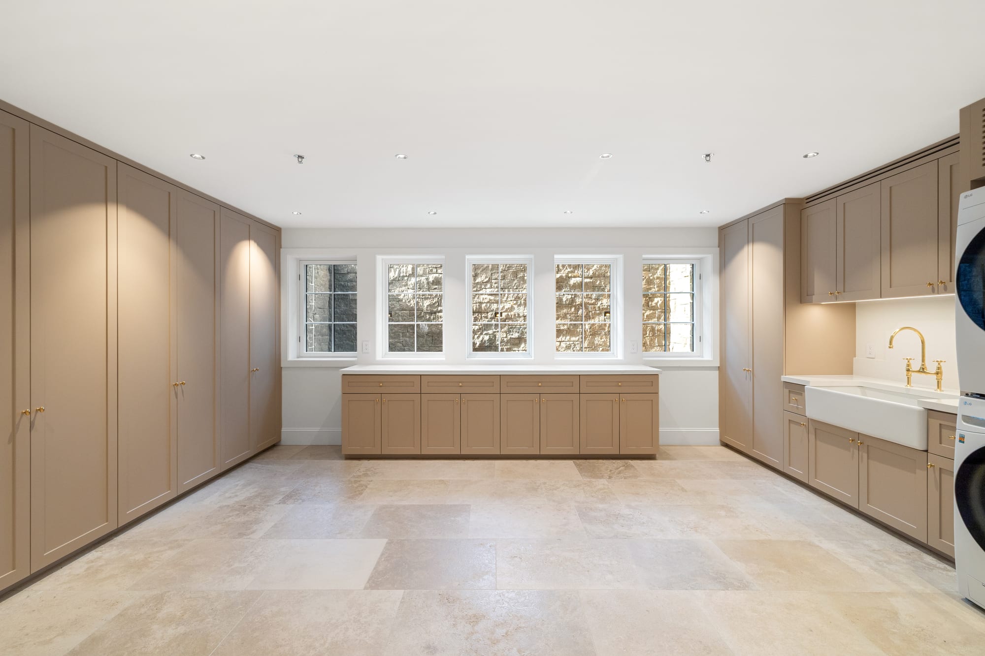 Laundry and mudroom in painted cabinetry with travertine floor and farmhouse sink.