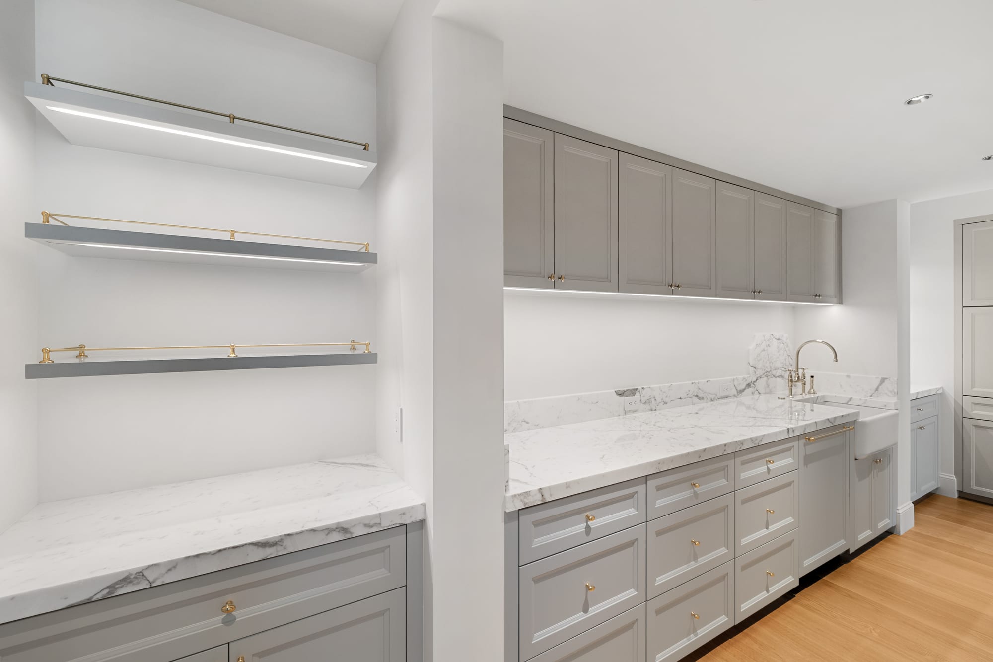 Butler's pantry with brass-edged floating shelves and marble counters on painted cabinetry.