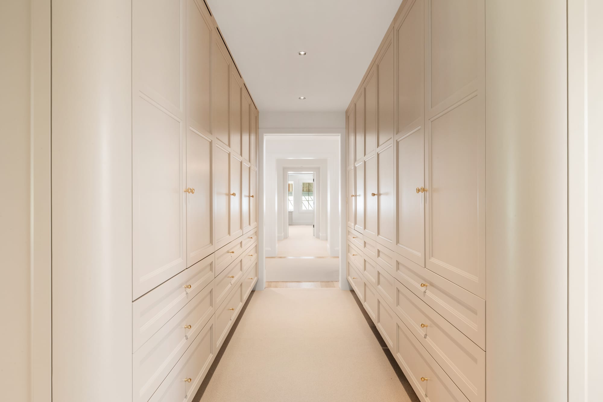 Dressing hall lined floor-to-ceiling with painted wardrobes, drawers and brass pulls.