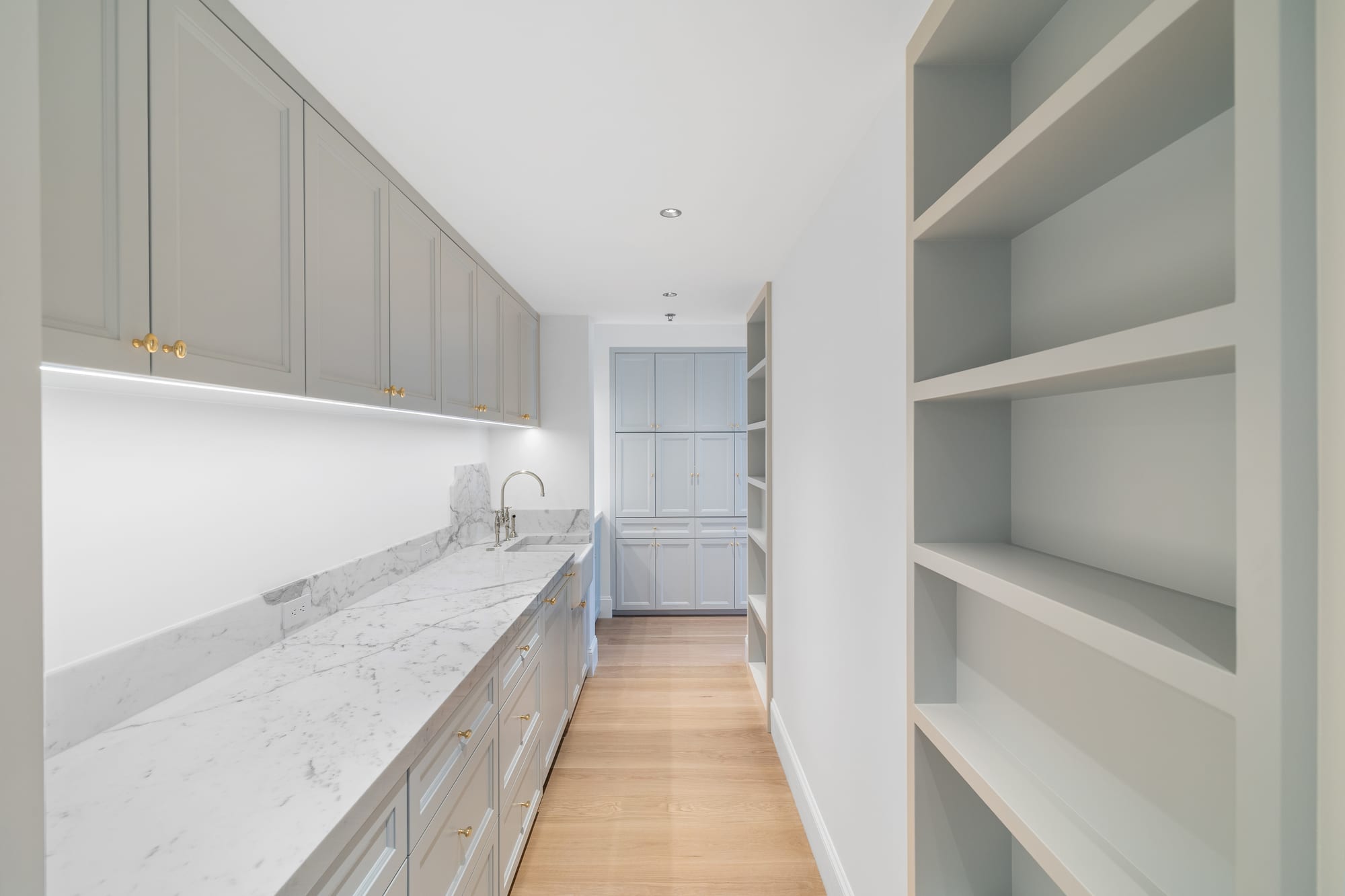 Butler's pantry in painted cabinetry with marble counters and integrated lighting.