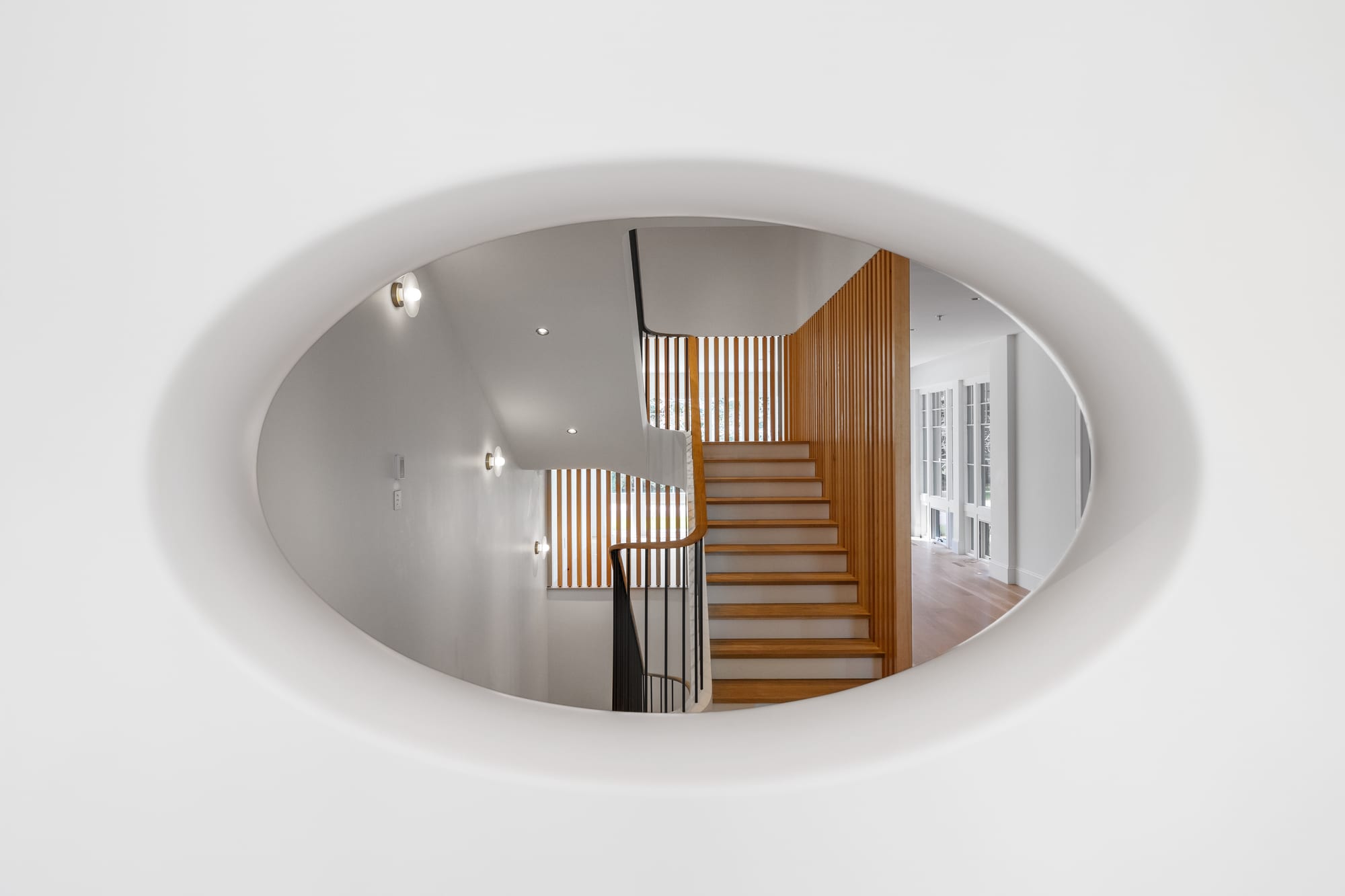 Oval ceiling opening framing the angled stair and white oak slat wall below.