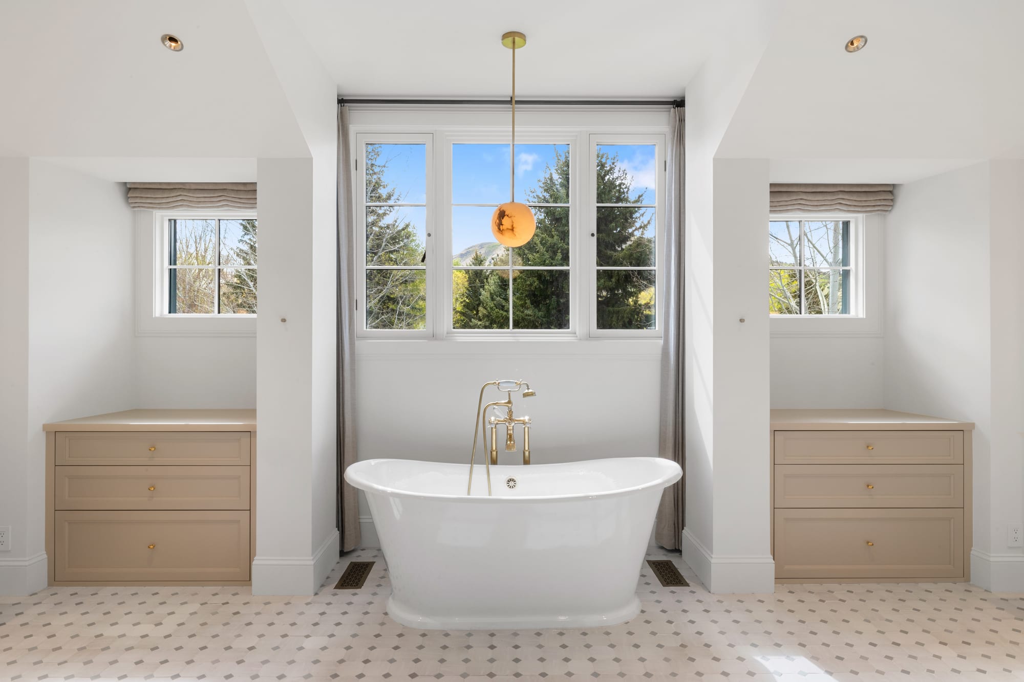 Freestanding tub framed by two built-in drawer chests in a mosaic-tiled bath.