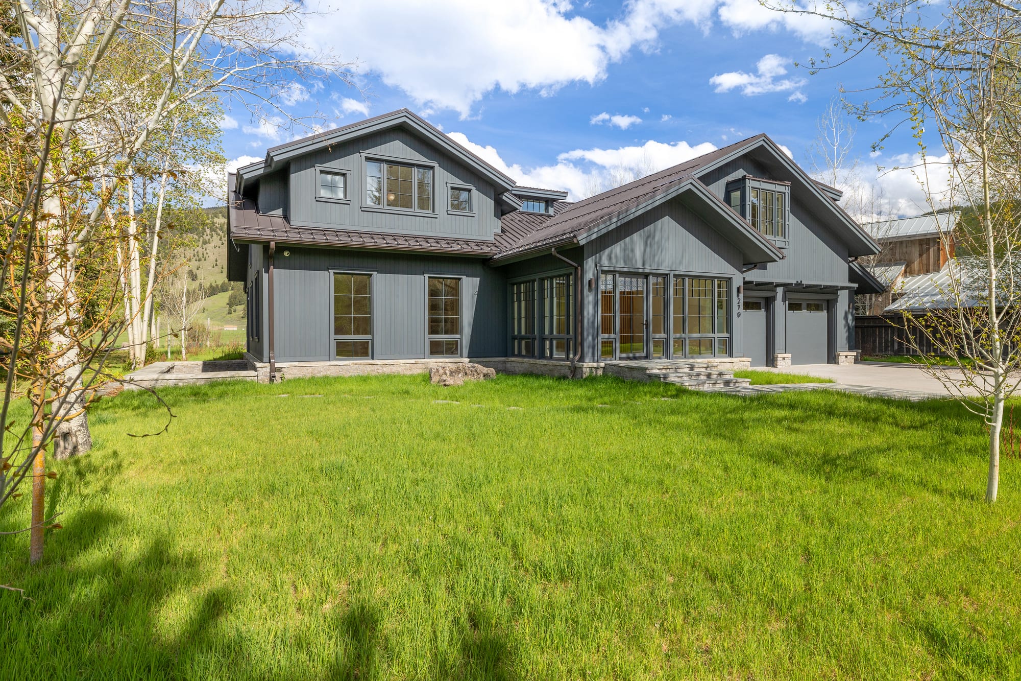 The house from the front lawn, charcoal siding against aspen and evergreen.