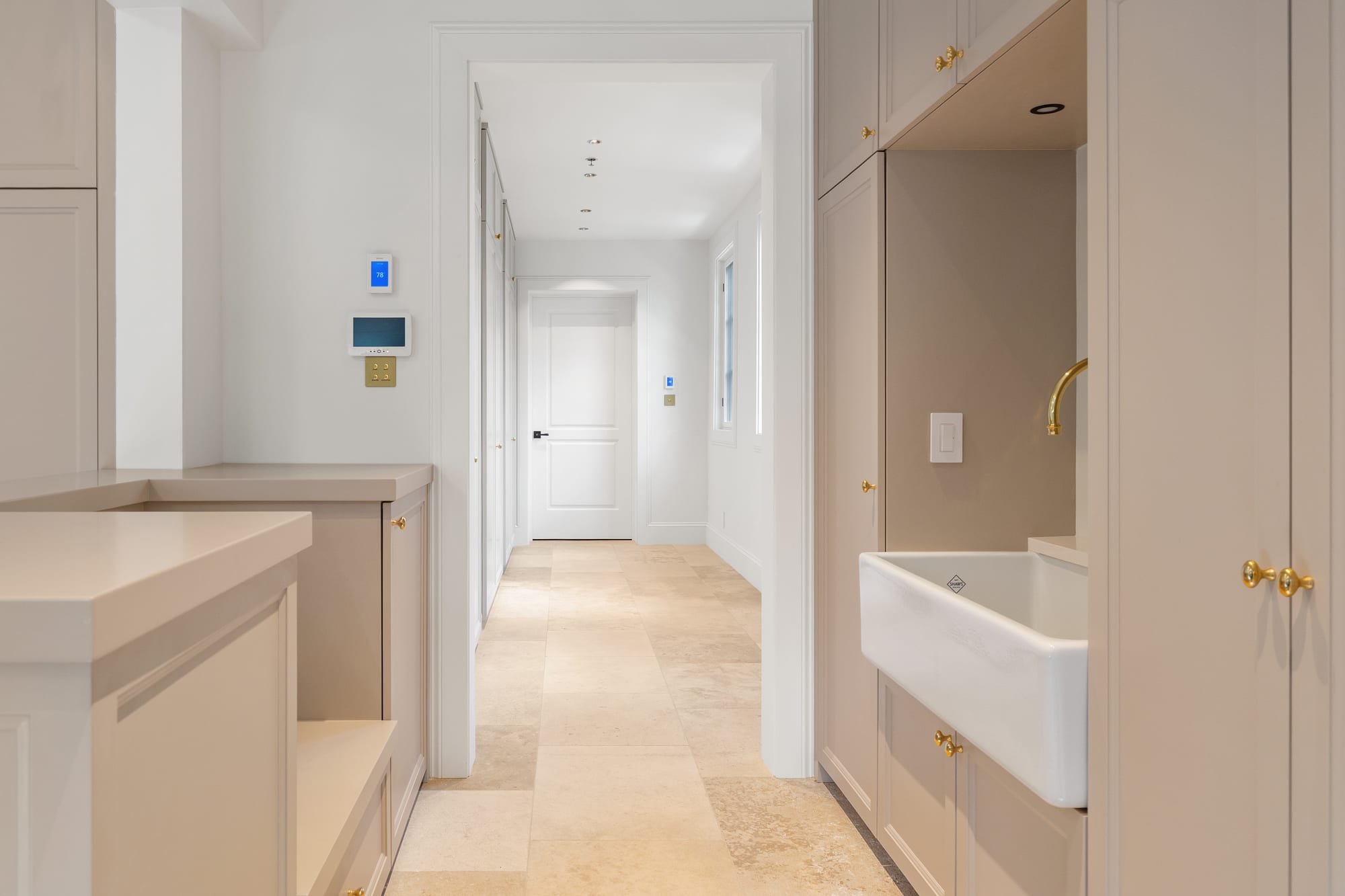 Butler's pantry corridor with farmhouse sink, painted cabinetry and travertine floor.