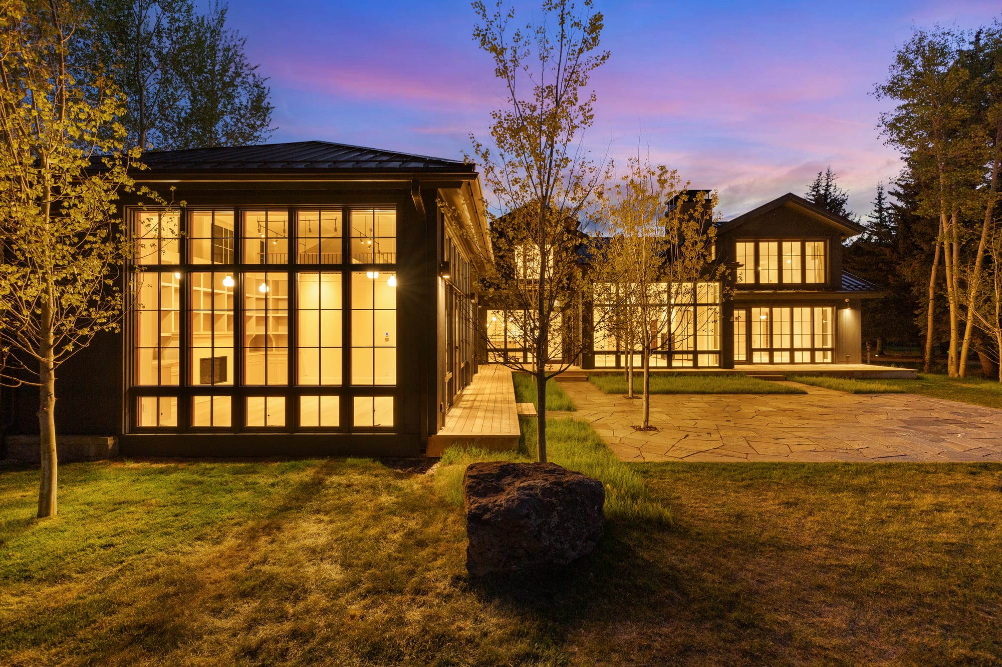 The studio wing glowing at dusk above the flagstone terrace.